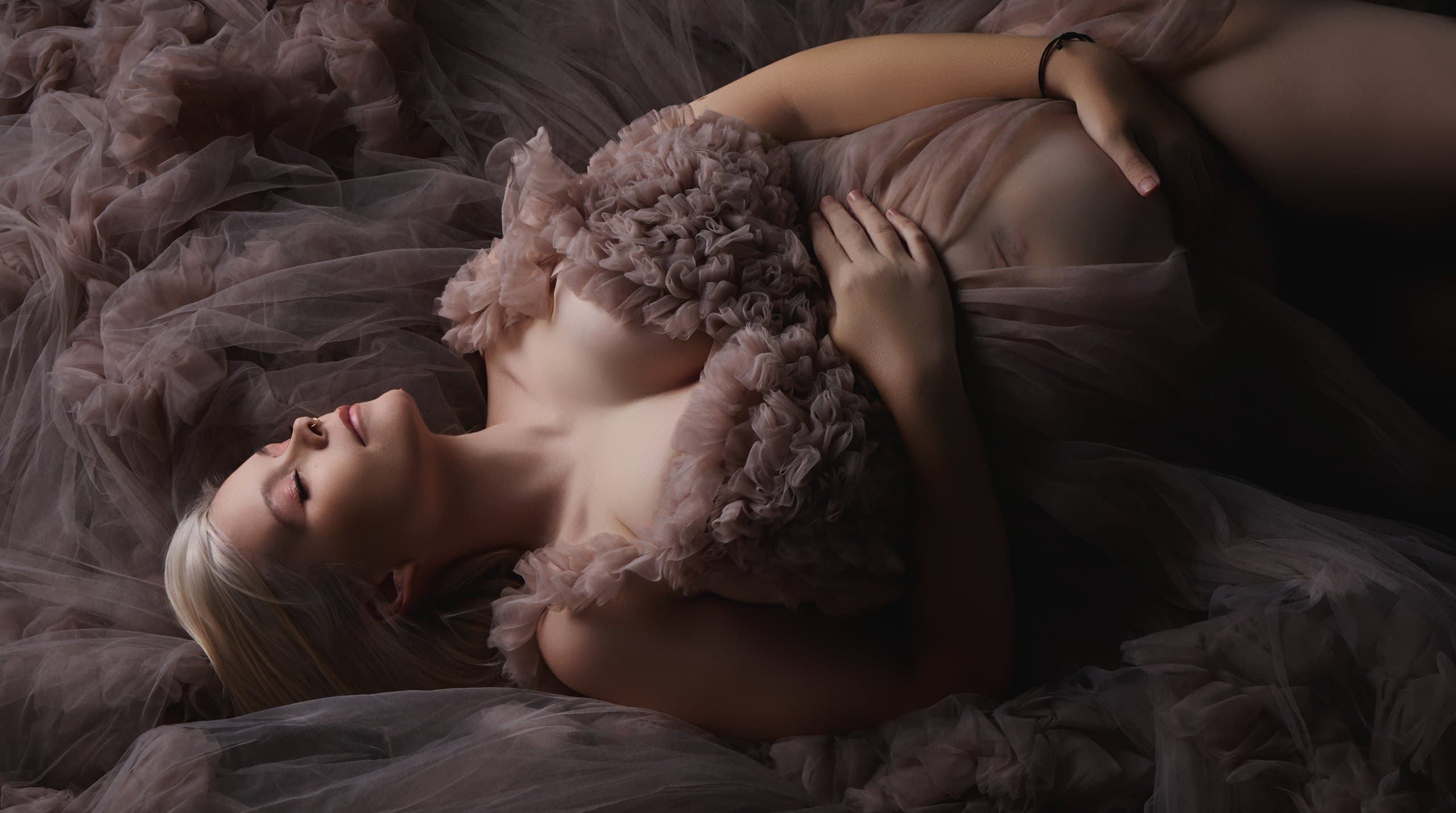 An expectant mother photographed in the studio under soft, sculpted light in a flowing couture gown