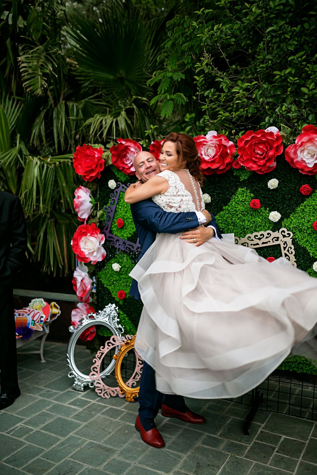 Wedding couple in front of a red rose wall at their Alice in Wonderland celebration