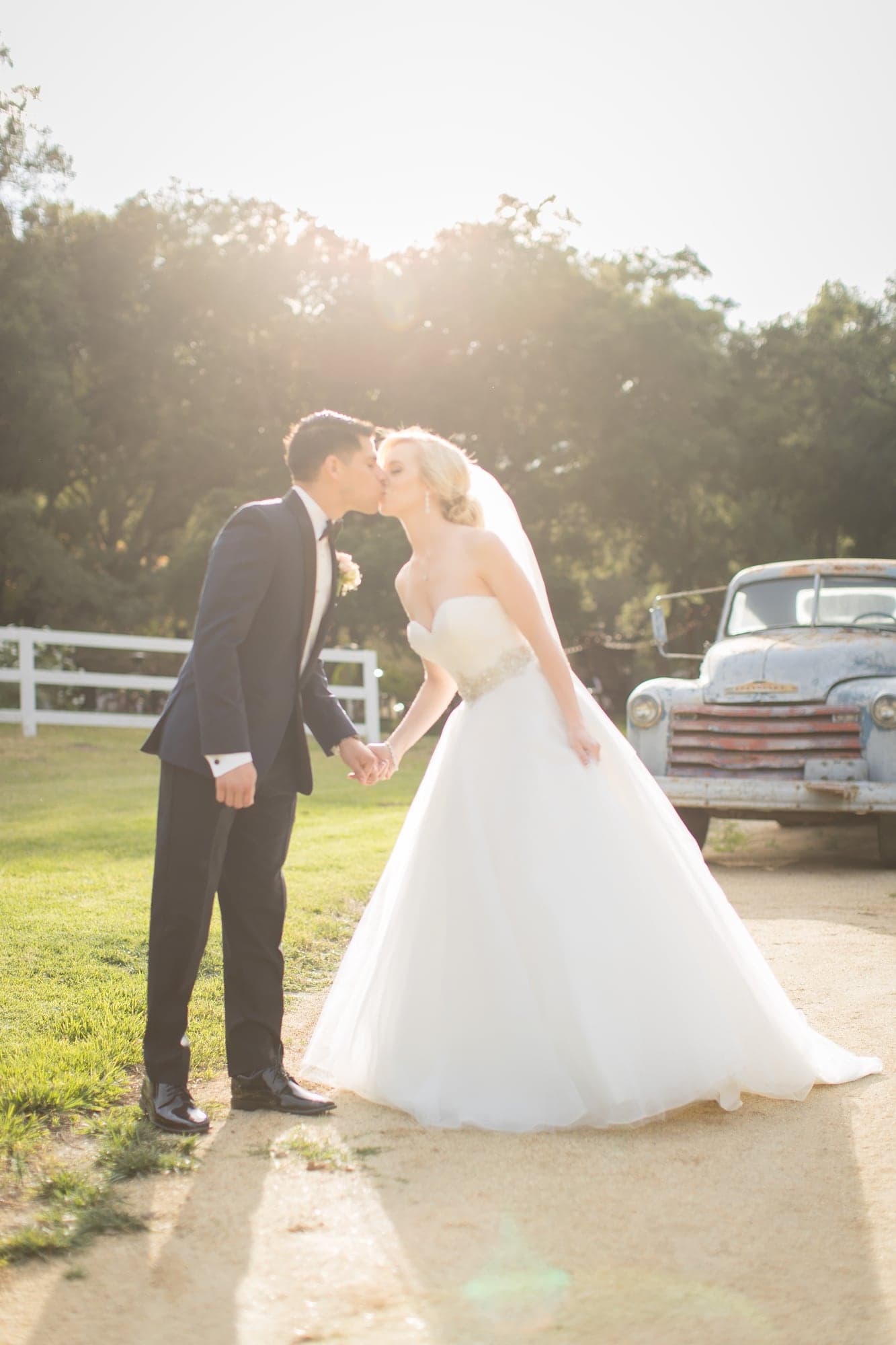 Krista and Oscar sharing a kiss beside a vintage truck at Circle Oak Ranch