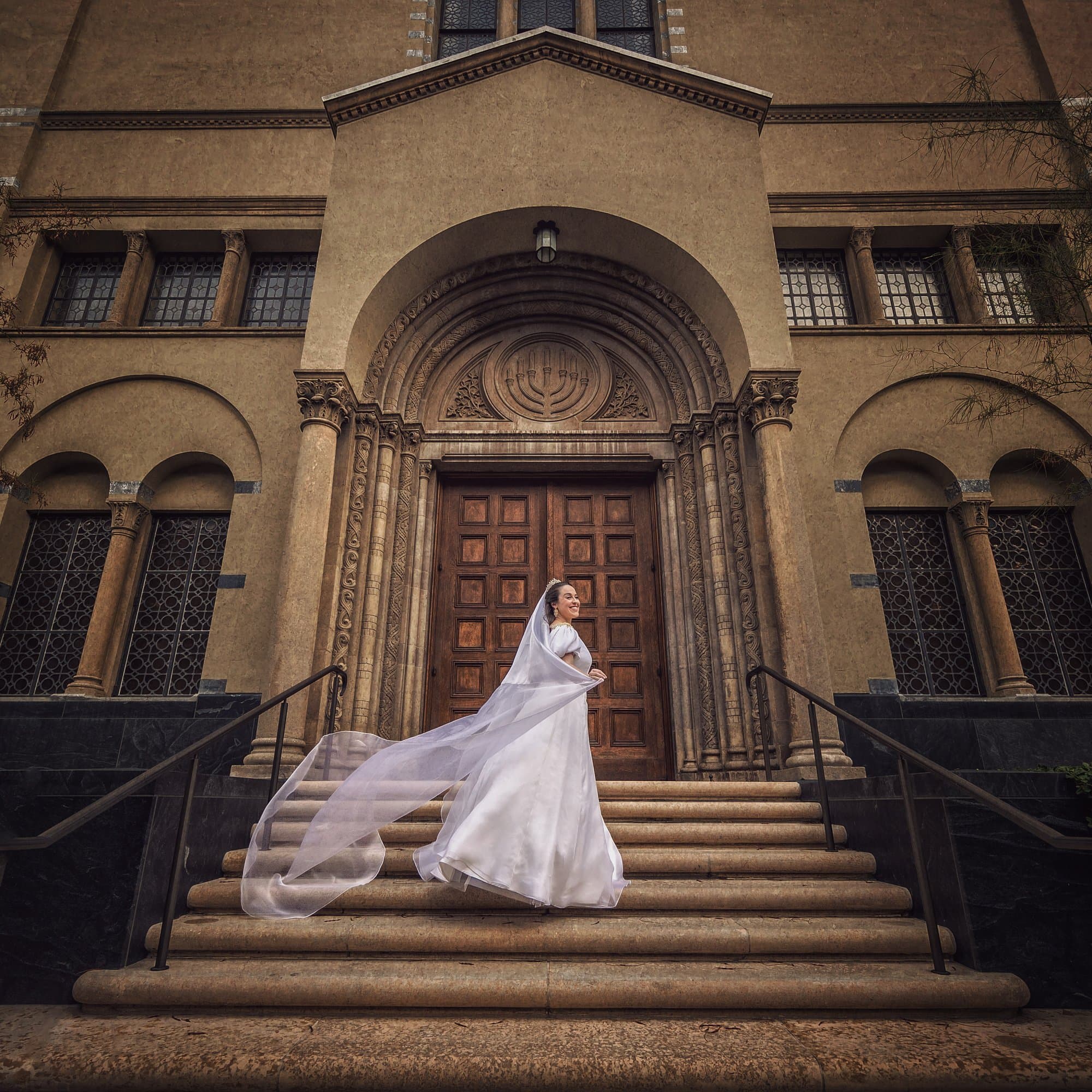 A bride mid-step on the stone staircase of a historic temple, her cathedral veil lifting behind her