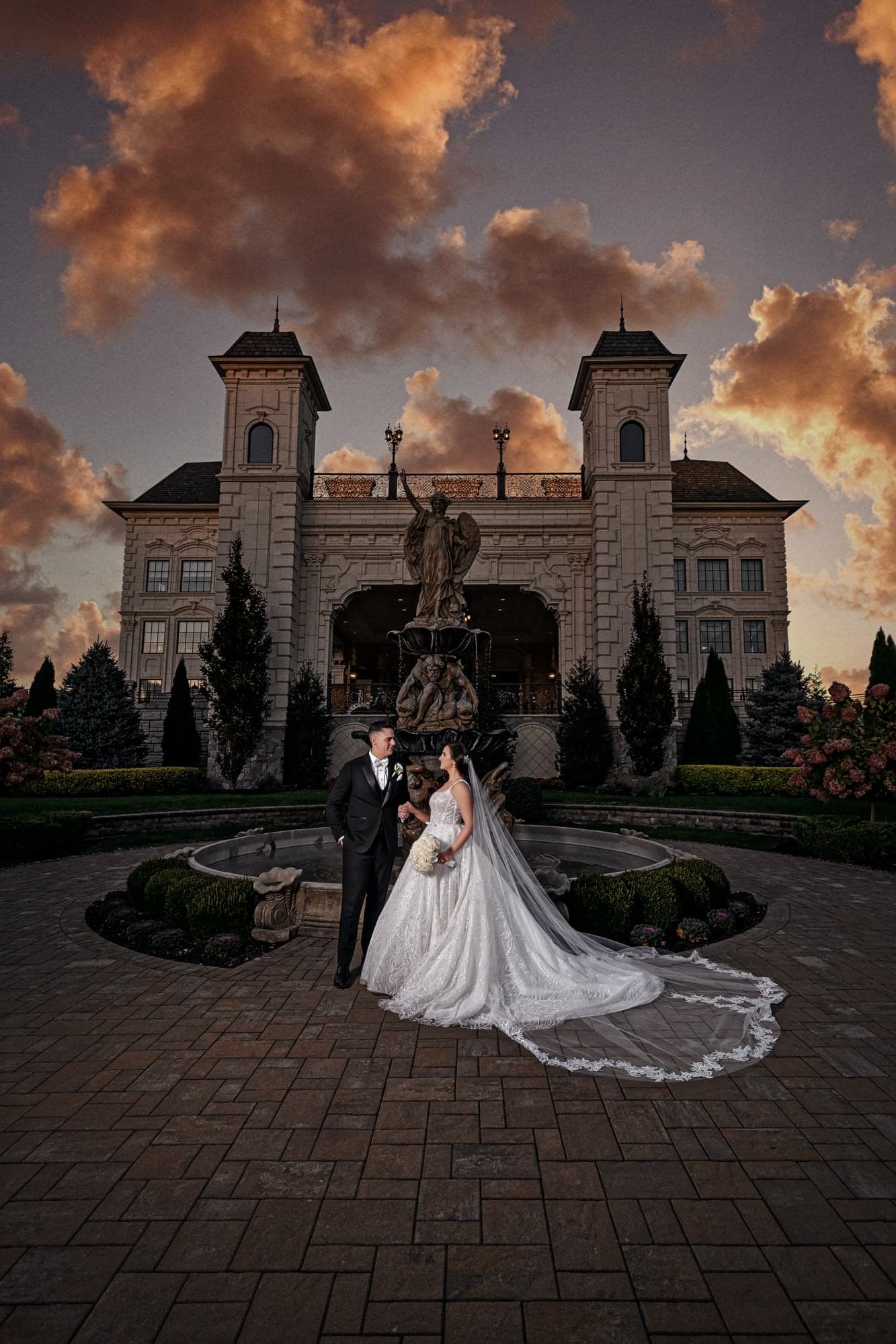 Christopher and Piera standing with a vintage white car in front of Legacy Castle at sunset