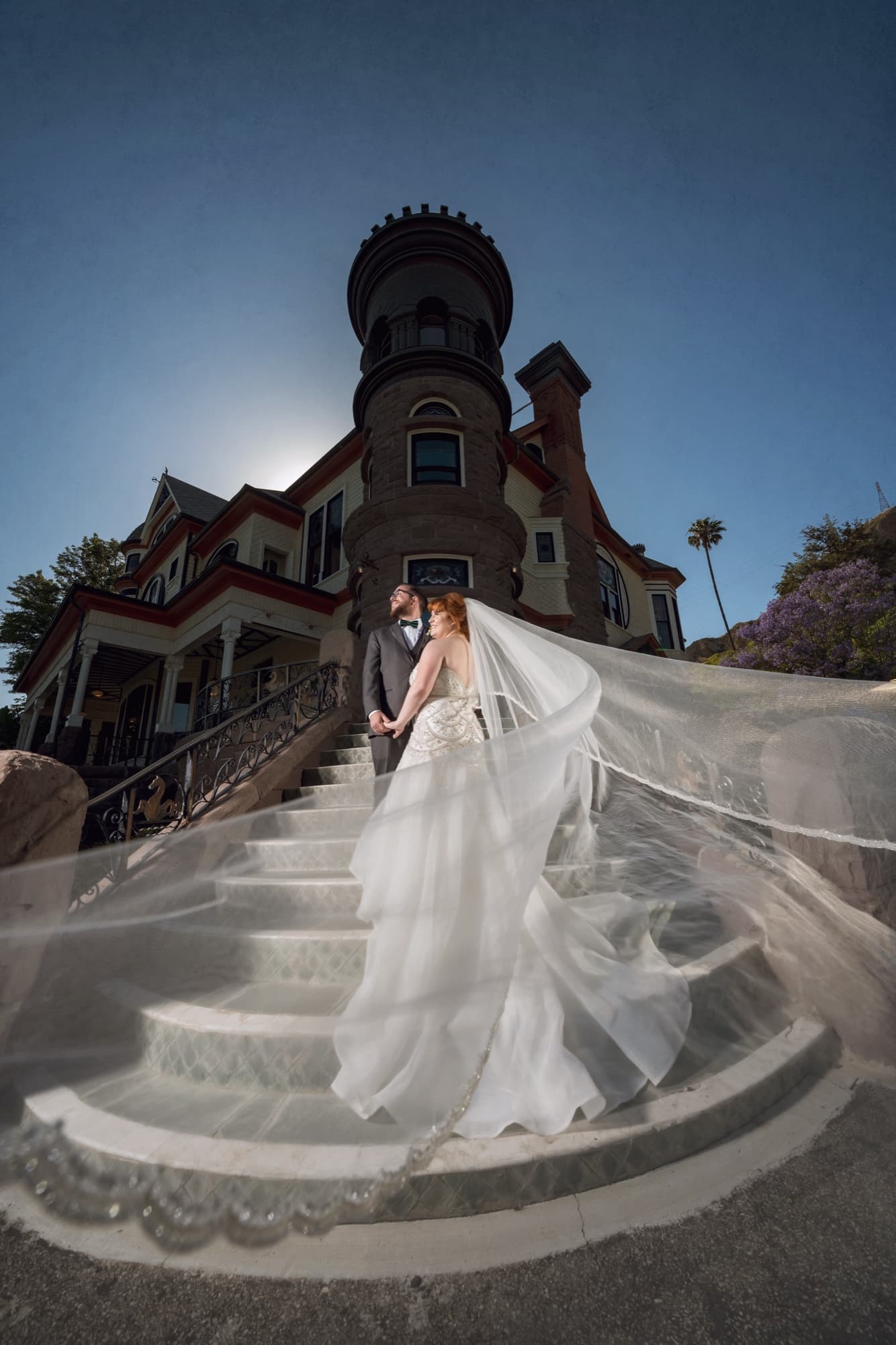 Michelle on the stone turret staircase of Newhall Mansion, her cathedral veil pouring down the steps beneath a sky of streaked clouds, photographed by Michael Anthony Photography