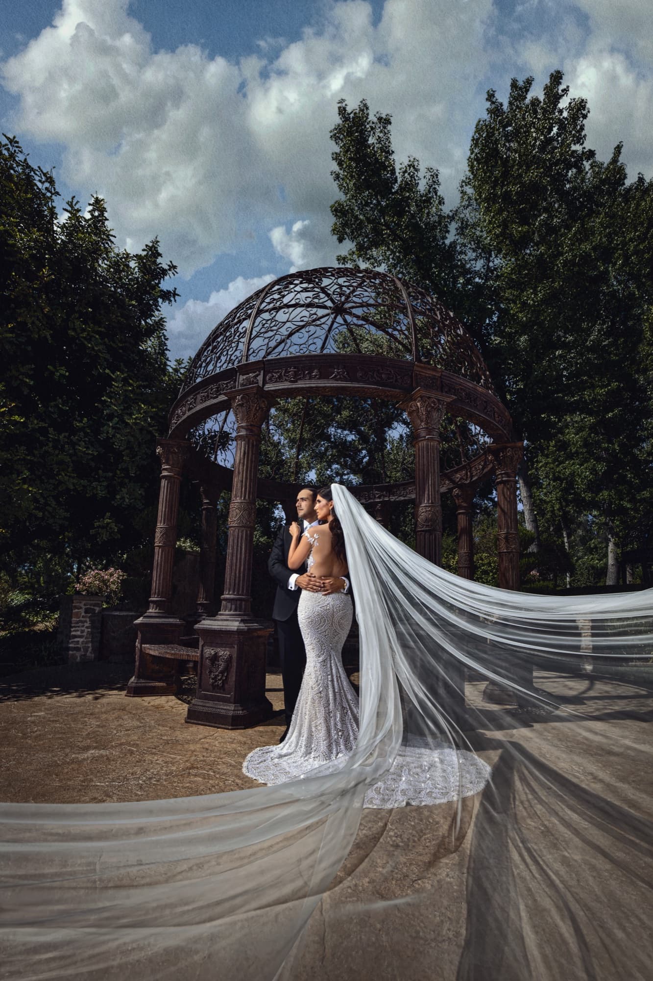 Christina at Saddlerock Ranch's iron gazebo, her cathedral veil cascading across the ground beneath a dramatic summer sky, photographed by Michael Anthony Photography