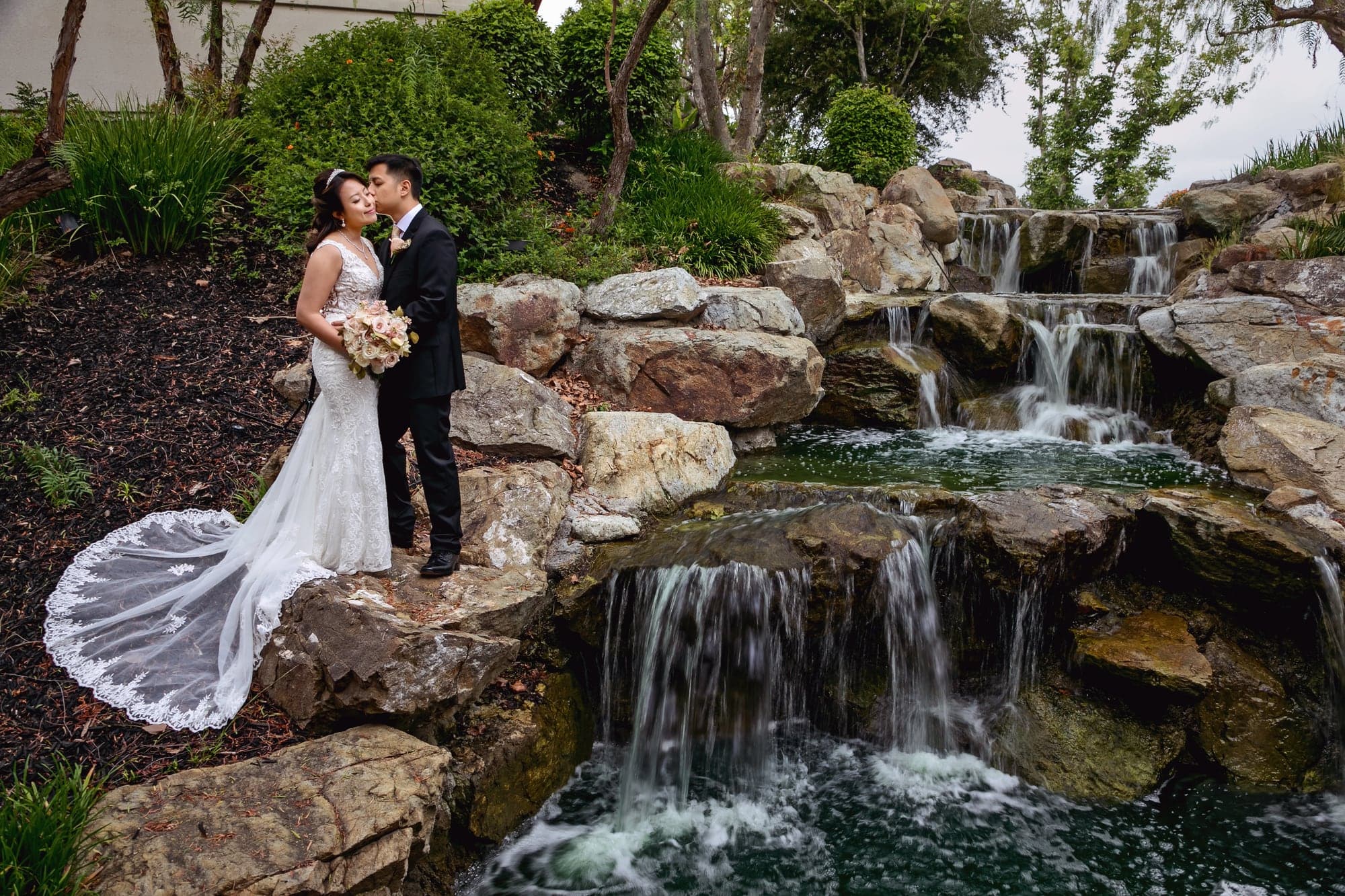 Wedding couple standing beside a garden waterfall