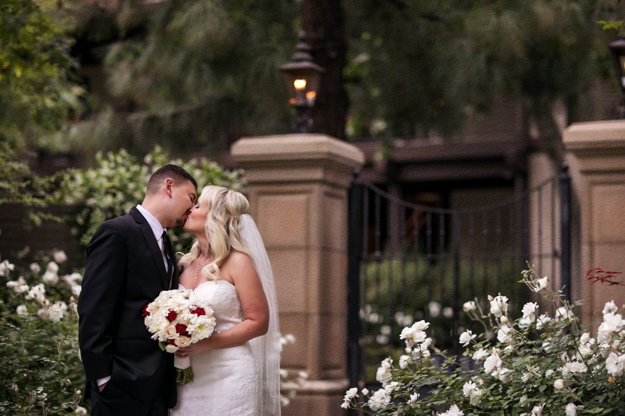 Gina and David embracing beside white roses at The Garland