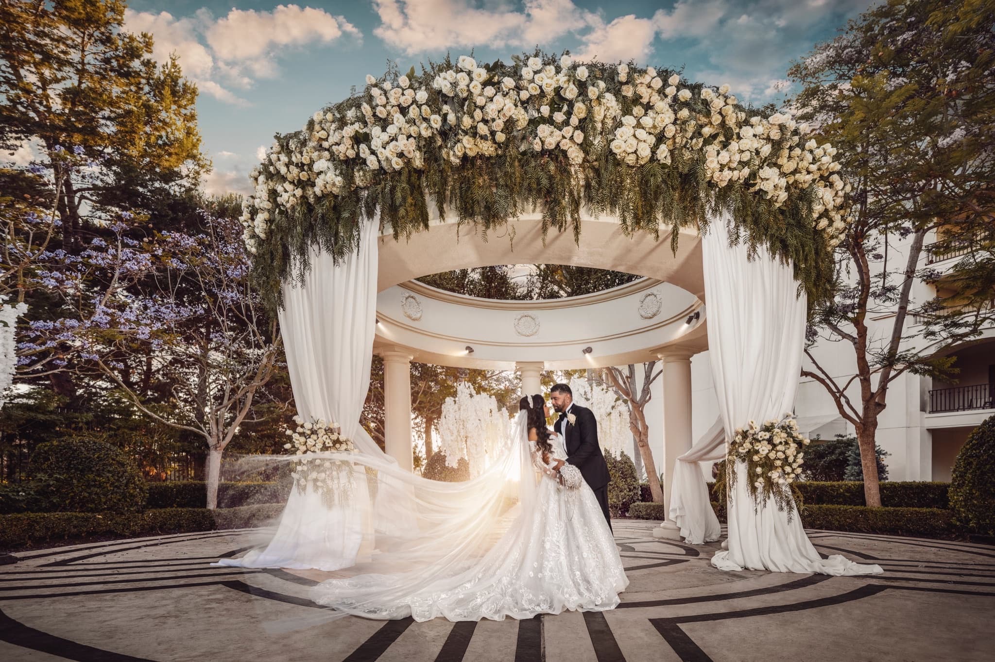 Shawni and Cash beneath the white-rose-crowned rotunda at the Waldorf Astoria Monarch Beach, her veil glowing in the backlight between the drapery, photographed by Michael Anthony Photography