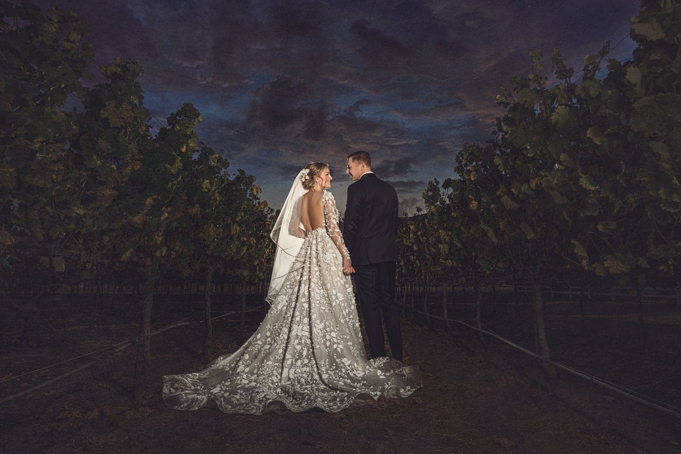 A wedding couple in a vineyard at dusk, the bride's long veil trailing, evoking a McKinney vineyard wedding