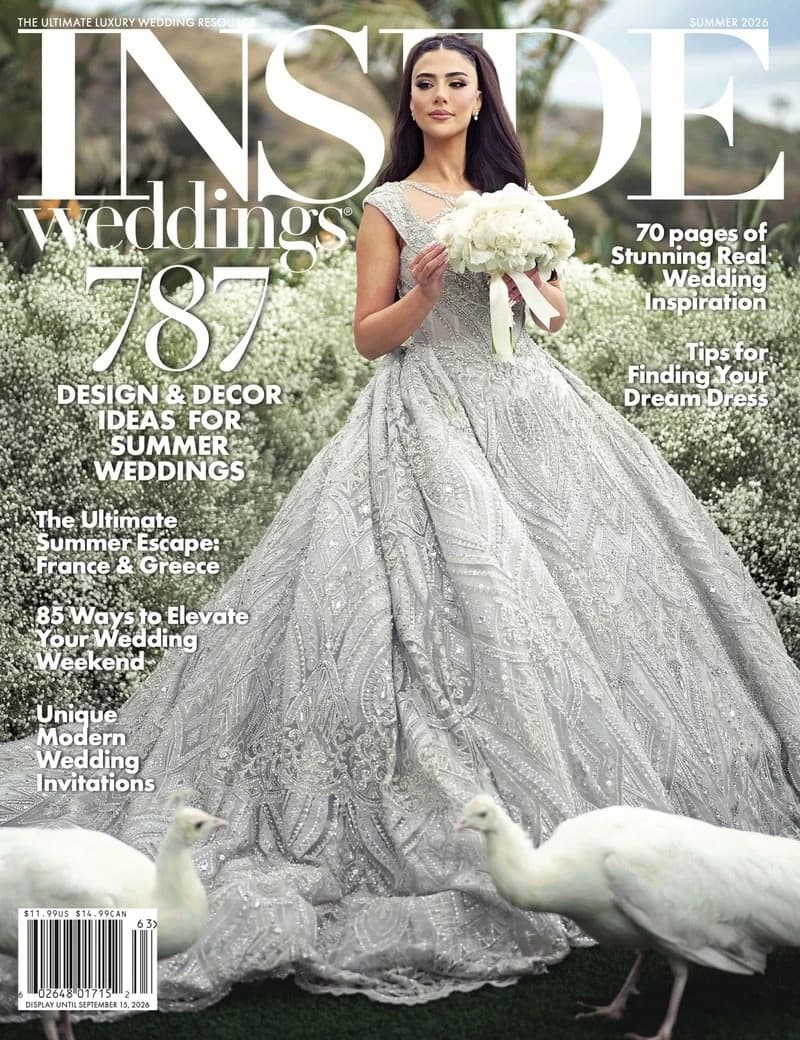 The Summer 2026 cover of Inside Weddings: a bride in a crystal-beaded silver ballgown holding a white bouquet, flanked by white peacocks in a garden of baby's breath, photographed by Michael Anthony Photography